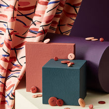 Load image into Gallery viewer, Brushstroke print viscose twill fabric hangs behind a display of blocks and buttons