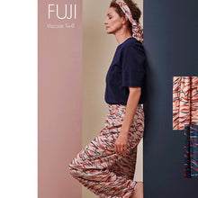 Load image into Gallery viewer, Side view if lady leaning on a wall with one leg bent, wearing trousers made with the Fuji Blush Viscose Twill fabric