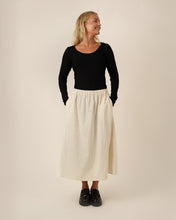 Load image into Gallery viewer, Model wears the Claude Skirt; an ankle length skirt with elasticated waistband, worn with plain long sleeved top tucked into the waistband. Hands in inseam side pockets