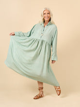 Load image into Gallery viewer, Lady wears a loose fit dress with top button up shirt, long sleeve with cuffs, with skirt gathered at waist, midi length