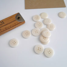 Load image into Gallery viewer, Scattering of 4-hole buttons displayed next to wooden ruler
