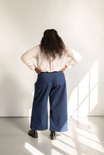Load image into Gallery viewer, Back view of model standing with hands on hips, wearing wide-leg trousers with patch pockets