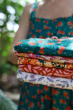 Load image into Gallery viewer, Lady holds out five square pieces of folded fabrics, all in different  designs