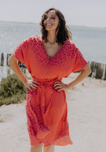 Load image into Gallery viewer, Lady at the beach with hands on hips wears the Transat Dress: a V-neck, short sleeved, knee length dress with waist tie