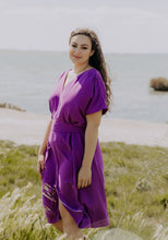 Load image into Gallery viewer, Lady at the beach wears the Transat Dress: a V-neck, short sleeved, knee length dress with waist tie