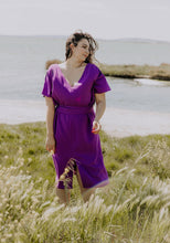 Load image into Gallery viewer, Lady at the beach wears the Transat Dress: a V-neck, short sleeved, knee length dress with waist belt