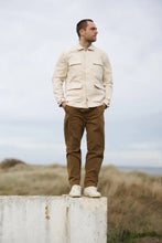 Load image into Gallery viewer, Male stands on wall wearing the Paynter Jacket, with four patch pockets with flaps at front, tabs with buttons at sleeves