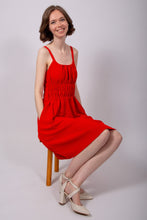 Load image into Gallery viewer, Model sits on chair, wearing a sleeveless, knee-length dress, with rounded neckline, elasticated waistline, hands in side pockets
