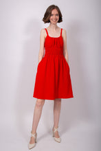 Load image into Gallery viewer, Model stands wearing a sleeveless, knee-length dress, with elasticated rounded neckline, elasticated waistline, hands in side pockets