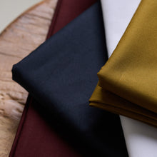 Load image into Gallery viewer, Oxford Cotton Fabric pieces in four different colours, folded and displayed on top of a wooden tabletop
