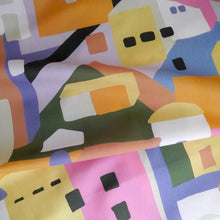 Load image into Gallery viewer, Cotton Lawn fabric with a colourful abstract pattern of geometric shapes resembling buildings, displayed with soft folds