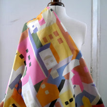 Load image into Gallery viewer, Cotton Lawn fabric with a colourful abstract pattern of geometric shapes resembling buildings, displayed draped on mannequin