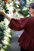 Load image into Gallery viewer, Image of lady picking a leaf on a hedge, shows off puffy sleeve, and gathered peplum detail