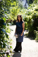 Load image into Gallery viewer, Lady wears a wrap dress over a pair of trousers, stands amongst green hedges