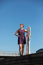 Load image into Gallery viewer, Lady stands on wooden platform wearing a sleeveless button up bodice jumpsuit with thigh length shorts