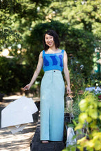 Load image into Gallery viewer, Lady stands holding a clip of paper patterns, wearing a maxi denim skirt with centre front split seam