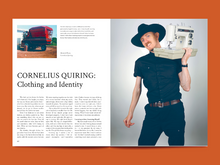 Load image into Gallery viewer, Two-page magazine spread features image of model holding up a sewing machine, next to page of text titled: "Cornelius Quiring: Clothing and Identity".