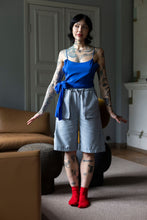 Load image into Gallery viewer, Model stands wearing a string strap vest top, paired with knee-length denim shorts with big pockets at hip level