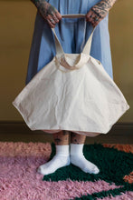 Load image into Gallery viewer, Lower view of model holding a trapezoid-shaped tote bag