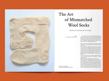 Load image into Gallery viewer, Magazine spread features photo of knitted sock with angles to form a square piece, alongside article titled: "The Art of Mismatched Wool Socks".