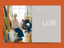 Load image into Gallery viewer, Two-page magazine spread, left side shows lady sat in an artist's studio. Right side features title text "Loïe"