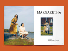 Load image into Gallery viewer, Two-page magazine spread, features images of 2 models out near a body of water, both wearing loose-fitting dresses, along with text reading "Margaretha".