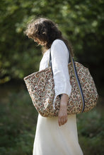 Load image into Gallery viewer, Model walking amongst green backdrop, carries a large quilted tote bag on shoulder