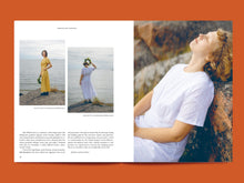 Load image into Gallery viewer, Two page magazine layout features text and images of models on rocks by the sea, wearing short-sleeved, ankle length dresses