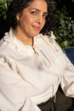 Load image into Gallery viewer, Lady sits wearing a long sleeve shirt with gathered ruffles at collar edge, and at shoulder seams