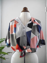 Load image into Gallery viewer, A short-sleeve button-front blouse with a geometric colour-block print, displayed on a mannequin torso.