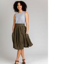 Load image into Gallery viewer, Lady stands wearing a gathered, knee-length Brumby skirt with hands in deep scoop pockets.