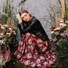 Load image into Gallery viewer, Lady crouches down amongst trees and flowers, wearing a long skirt made with Peony Rust EcoVero Viscose fabric