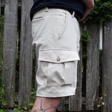 Load image into Gallery viewer, Side view of man wearing cream coloured cargo shorts with patch pocket with flap and button. Worn with a leather belt.