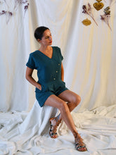 Load image into Gallery viewer, Lady wearing an asymmetrical, 3-buttoned top and shorts playsuit in a green fabric with pleats detail at front shoulder.