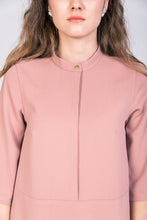Load image into Gallery viewer, Close up of neckline detail - a gold button fastens small stand collar, of lady wearing tunic style dress in pink fabric.