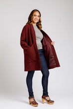 Load image into Gallery viewer, Lady wears a knee-length lined Hovea Coat with hand in deep slanted pocket at waist level