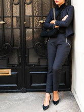 Load image into Gallery viewer, Lady with arms crossed leant in a corner, wearing smart fitted LouLou trousers with white piped detail at pocket seams.