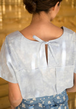 Load image into Gallery viewer, Back view of lady wearing a short sleeve top with inverted box pleat into a yoke, open at centre-back, fastened with knotted ties