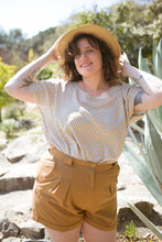 Load image into Gallery viewer, Lady stands wearing a scoop-neck, short sleeved Palma top and shorts with straw hat