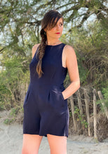 Load image into Gallery viewer, Lady wears a plain Luz jumpsuit with hands in pockets, pleats at waistline