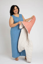 Load image into Gallery viewer, Lady holds a Hovea quilted jacket turning sleeve inside out to reveal a reversible jacket