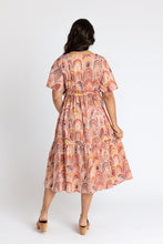 Load image into Gallery viewer, Back view of lady wearing Protea dress with one hand in pocket, one holding out tiered skirt