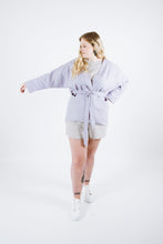 Load image into Gallery viewer, Lady wears Juno Jacket tied at waist, holds out right arm to show dolman sleeve