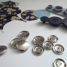 Load image into Gallery viewer, 23mm metal cover button blanks displayed next to cover tool and circular pieces of fabric