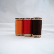 Load image into Gallery viewer, Wooden reels of organic cotton sewing thread in Tangerine, Ruby Red and Mid Brown colours