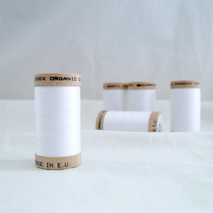 Five wooden reels of Organic Cotton sewing thread in White colour.
