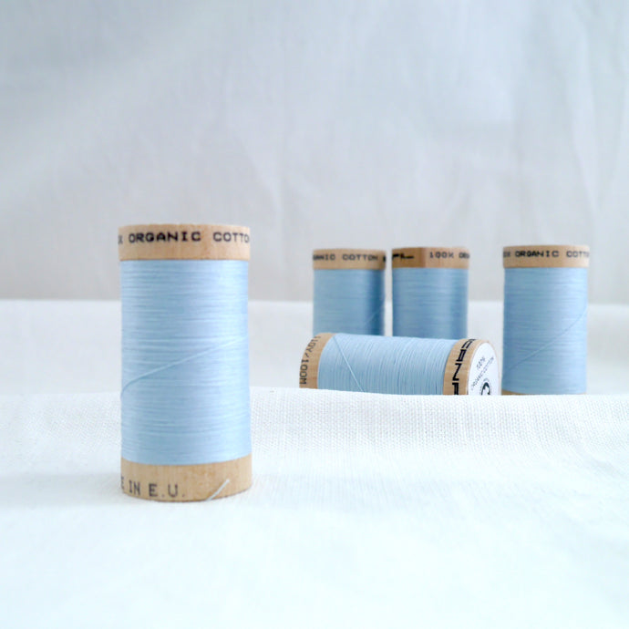 Five wooden reels of organic cotton sewing thread in pale blue.