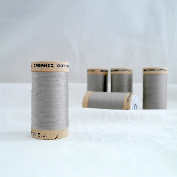 Five wooden spools of organic cotton sewing thread in Sand, a grey beige colour.