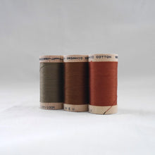 Load image into Gallery viewer, Three wooden reels of organic sewing cotton threads in khaki, acorn brown, and copper colours.