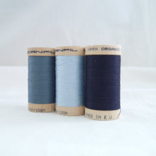 Load image into Gallery viewer, Three wooden reels of organic cotton sewing thread in three different shades of blue.